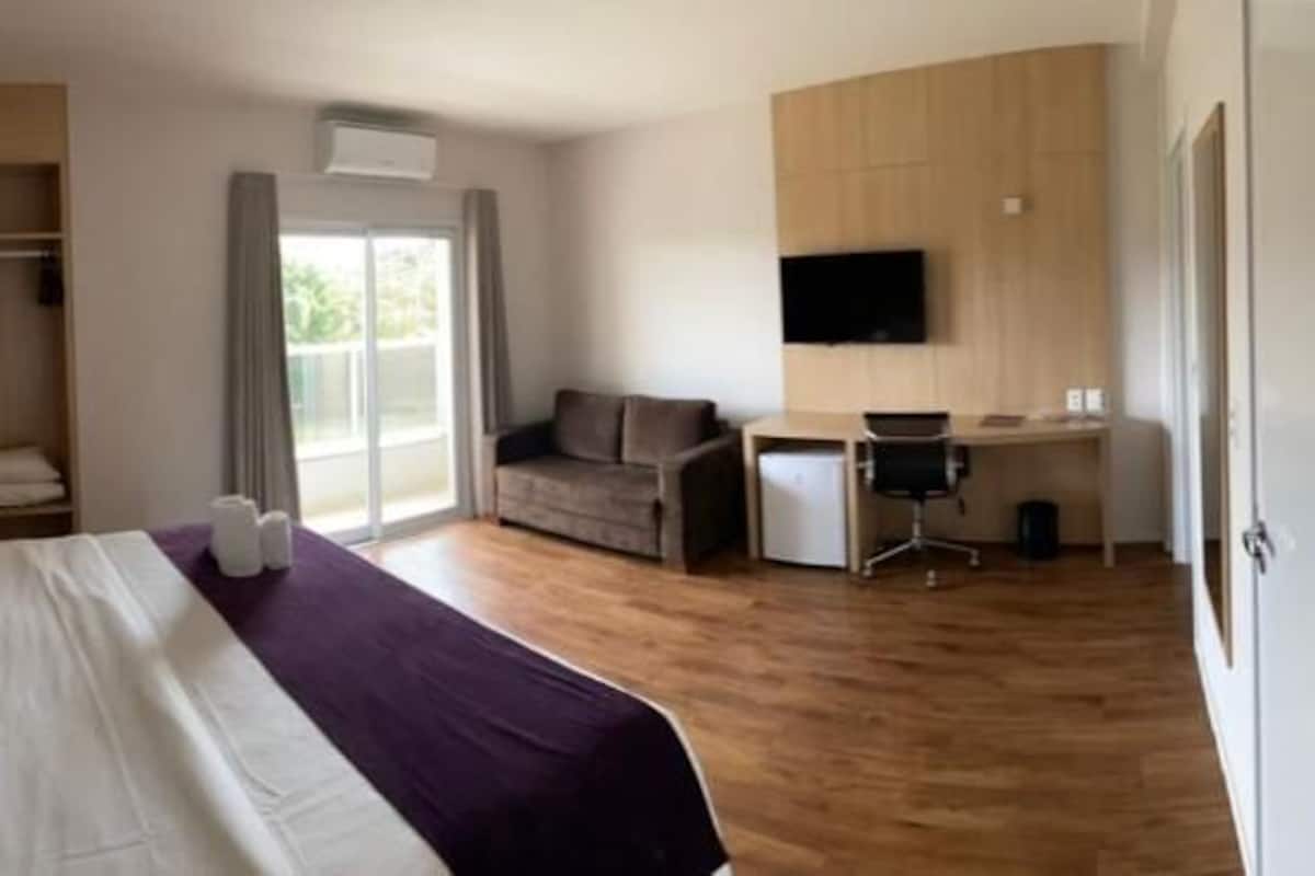 A hotel room with a bed, a desk, a chair, a television, and a wardrobe.
