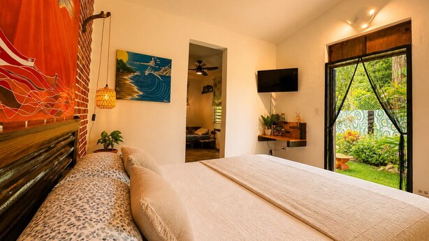 Ein Schlafzimmer mit Bett, Fernseher, Gemälde und Blick ins Freie.