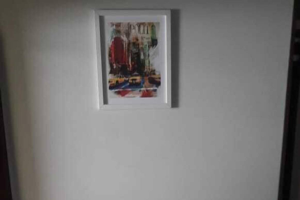 Ein ordentlich bezogenes Bett mit weißer Bettwäsche und einem grünen Überwurf, ein gerahmtes Bild an der Wand und eine Backsteinwand links.