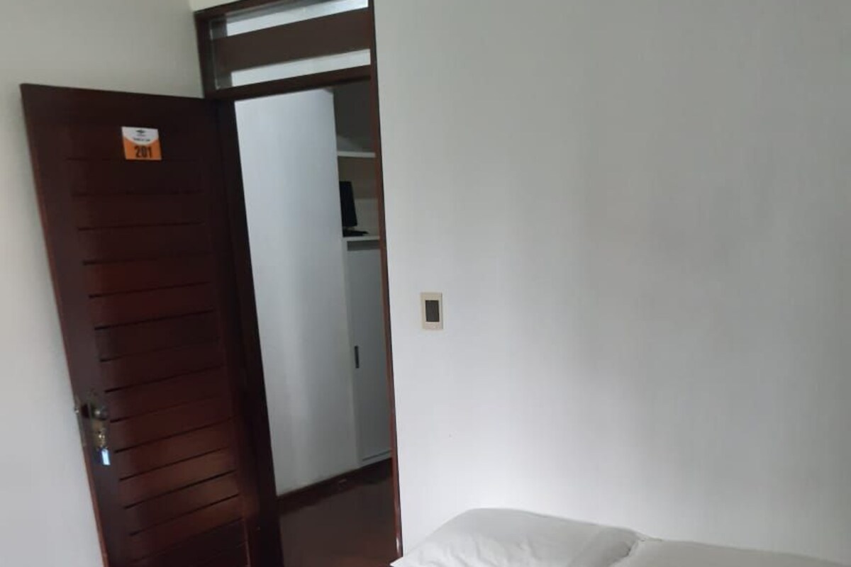 A hotel room with a bed, a blue bedspread, white pillows, and a pair of towels folded on the bed.