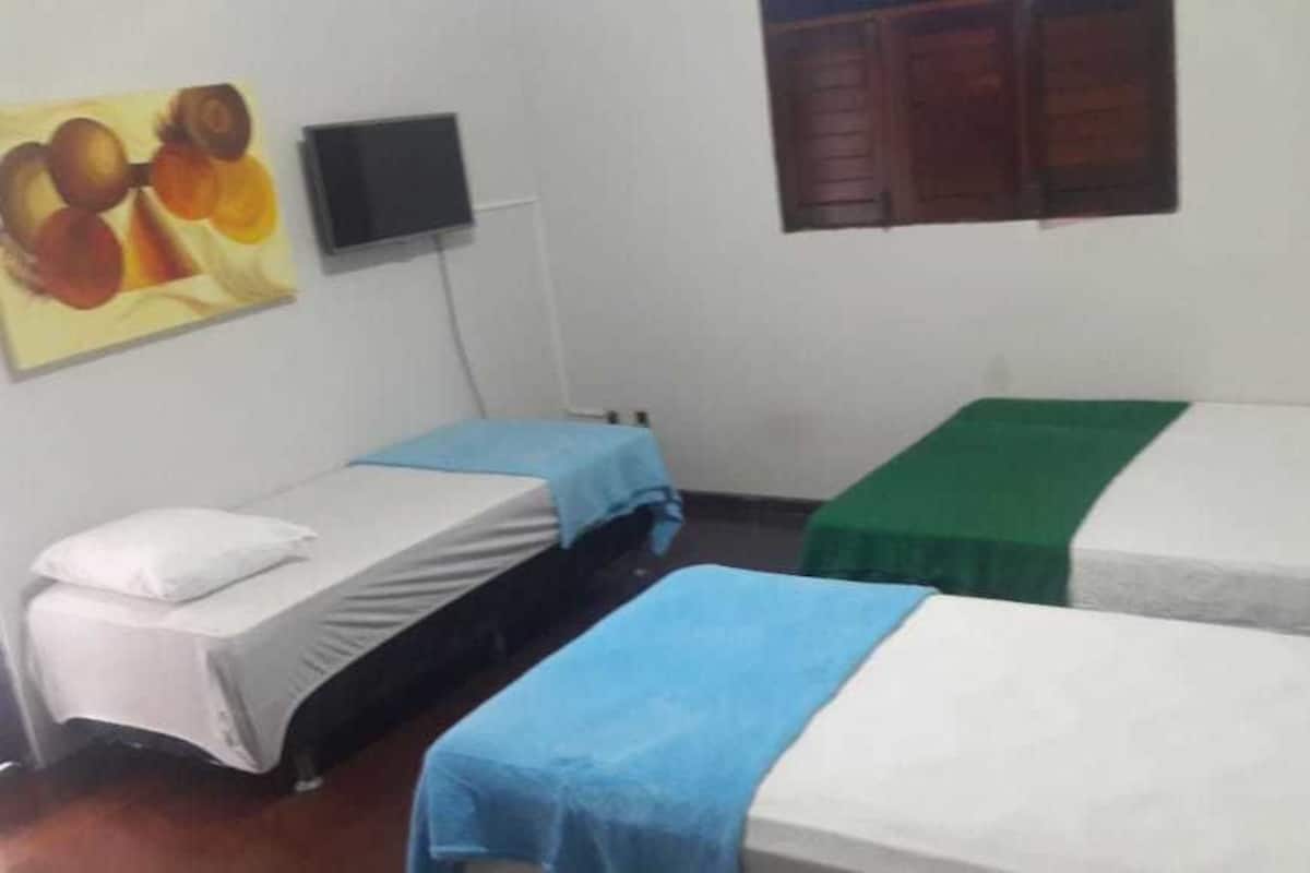 Ein Zimmer mit drei Einzelbetten, jedes mit einer andersfarbigen Bettdecke. An der Wand über den Betten ist ein Flachbildfernseher angebracht.