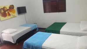 A room with three single beds, each with a different colored bedspread. There is a flat-screen TV mounted on the wall above the beds.