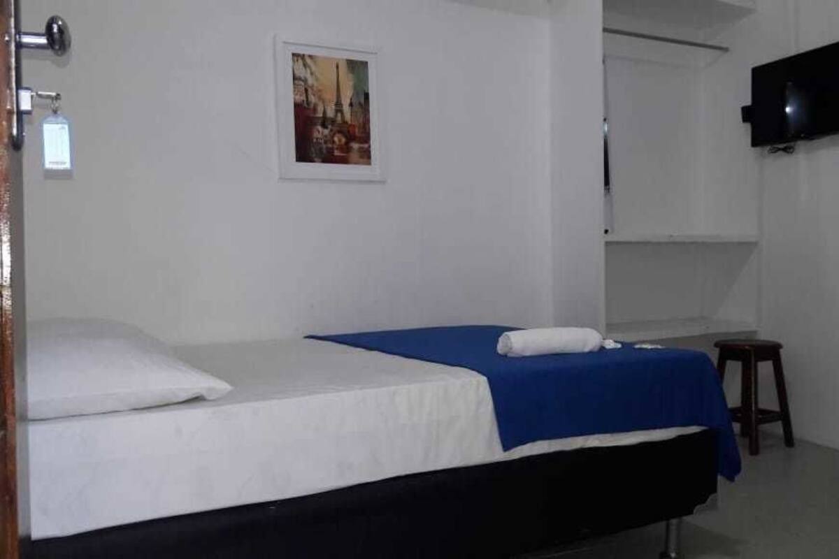 Ein Zimmer mit einem Bett, einem Schreibtisch, einem Sessel, einem Fernseher und einem Bild an der Wand.