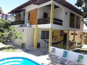 A two-story house with a swimming pool, outdoor seating, and a hammock.