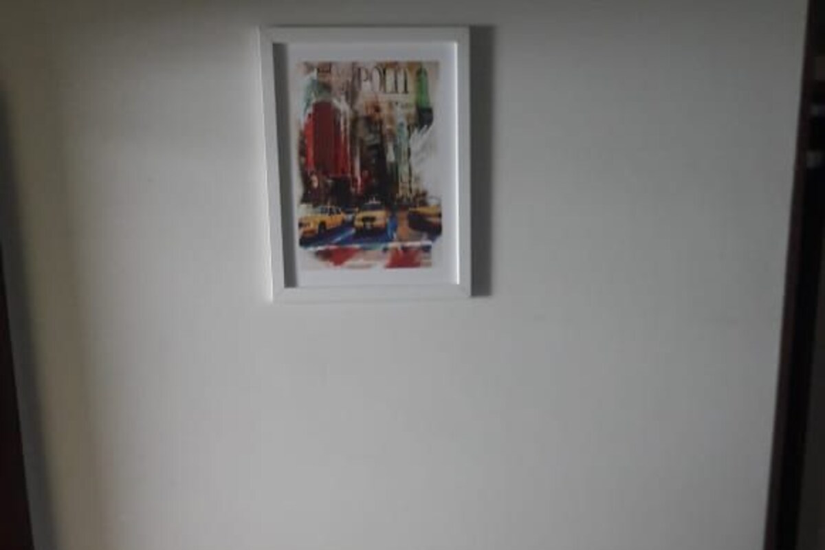 A neatly made bed with white linens and a green bedspread, a framed picture on the wall, and a brick wall to the left.