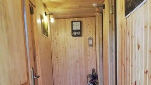 A wooden hallway with a clock on the wall, a chair with flowers, and a door on the left. - Agro Guesthouse Korena (Tkibuli)