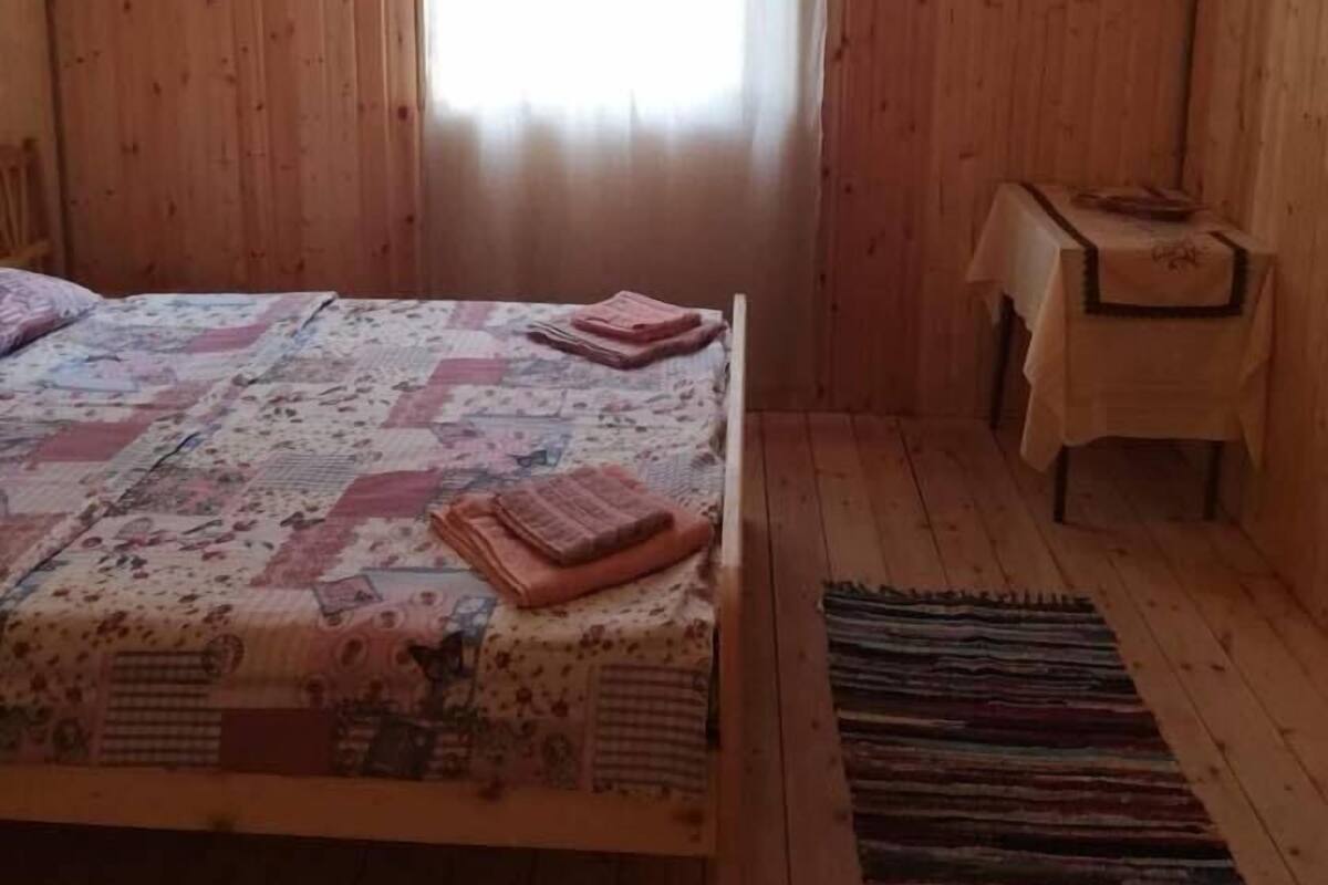 A wooden room with a bed, a small table, and a window.