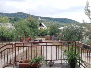 A balcony with a view of a house and trees, surrounded by a metal railing. - Agro Guesthouse Korena (Tkibuli)