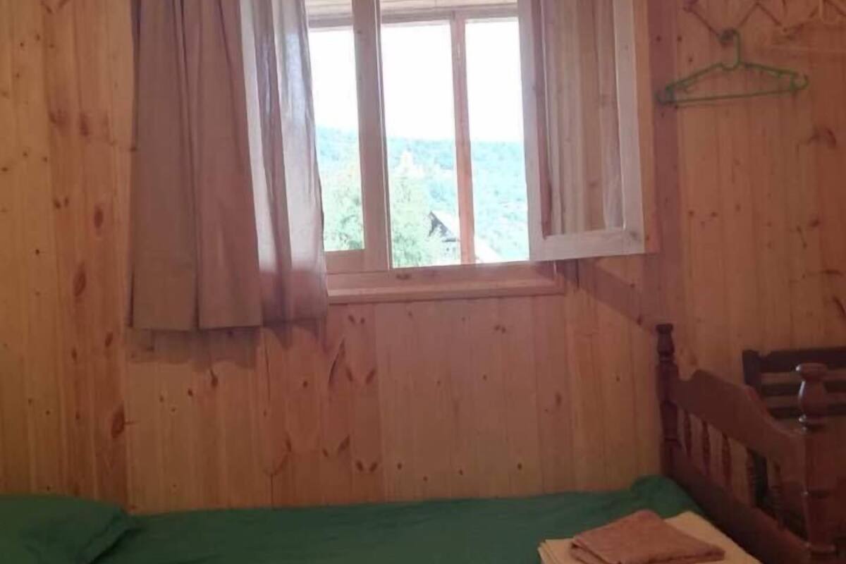 A wooden cabin room with a bed, a window with curtains, and a green hanger on the wall.