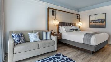 A bedroom with a bed, a sofa, a nightstand, a wall-mounted lamp, and a framed picture.