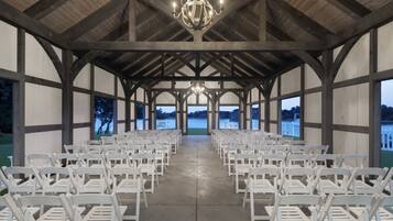 An indoor venue with a high ceiling and wooden beams, featuring rows of white chairs arranged for an event.