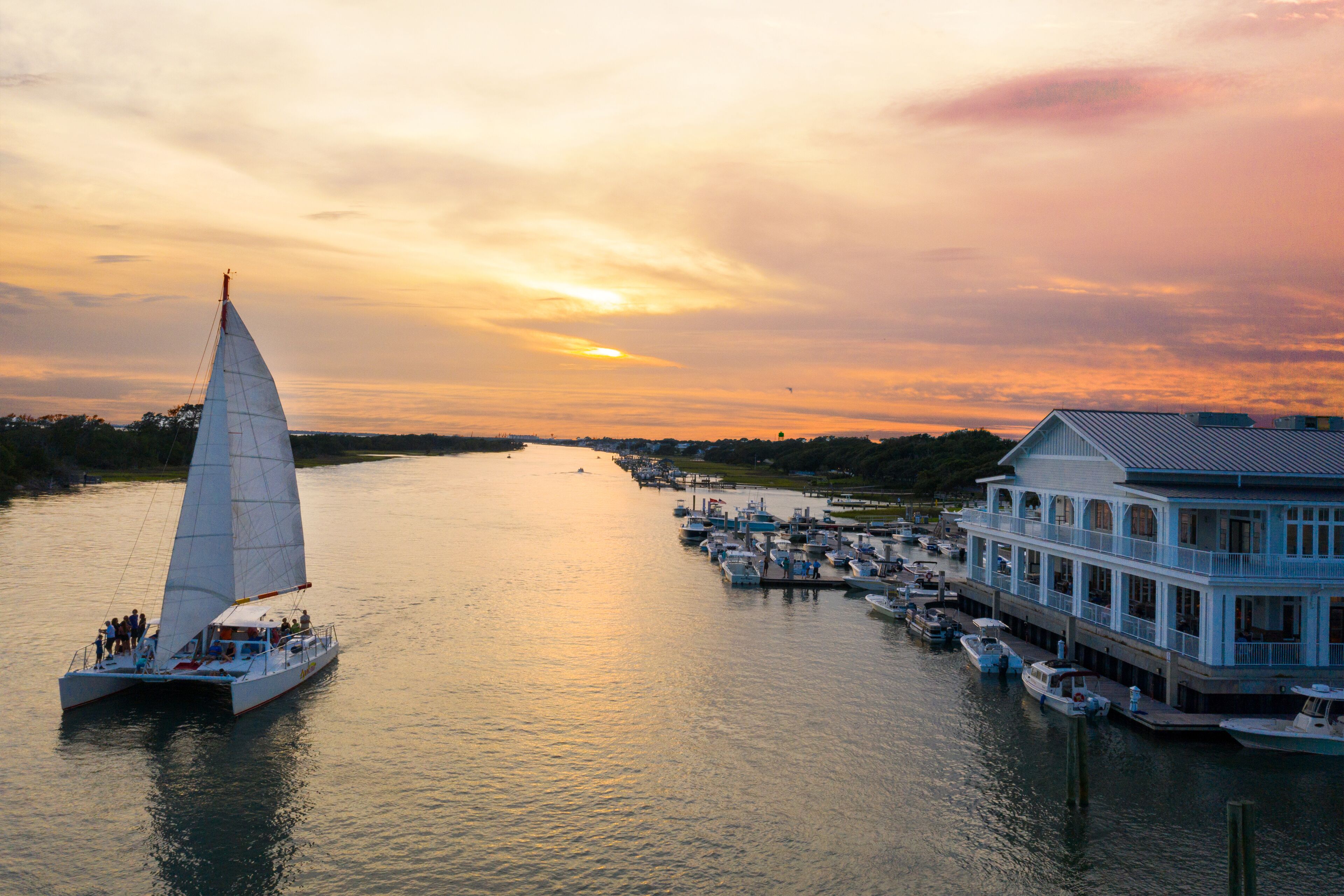 A sailboat on a calm river with a docked house on the right.