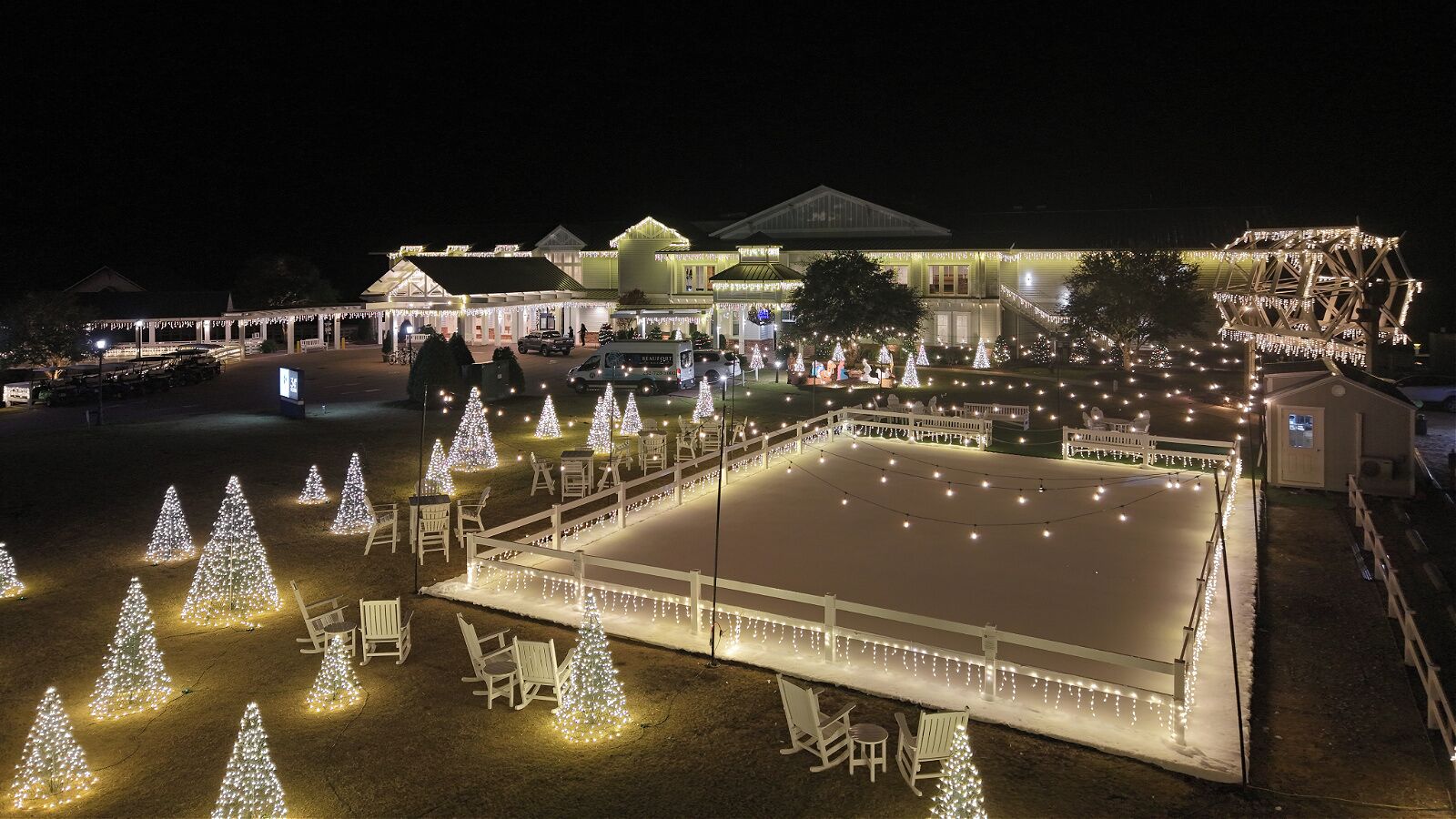 Un espacio interior amplio y abierto con una zona de estar central, rodeado de vallas blancas y árboles de Navidad.