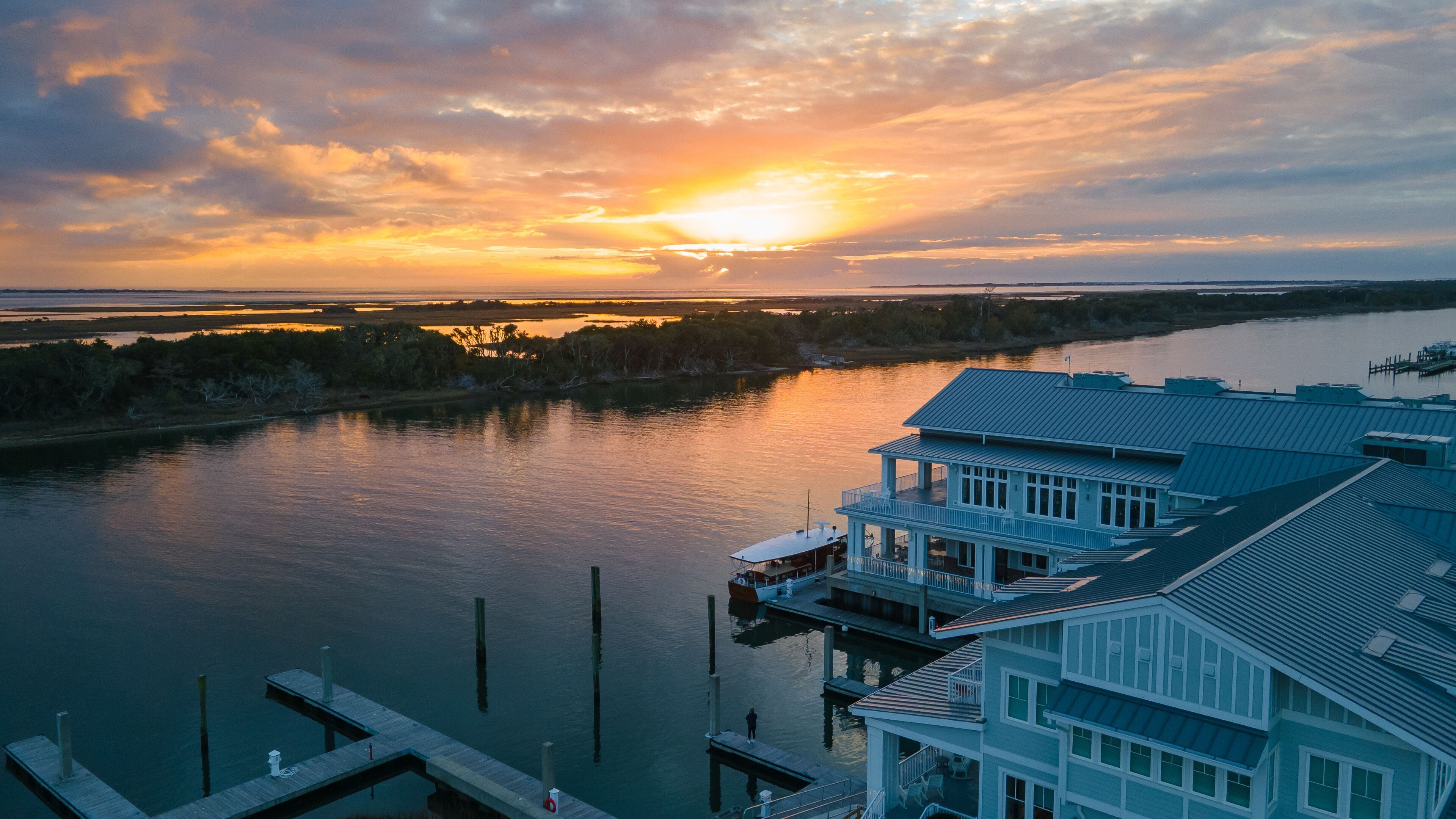 A waterfront property with a dock, a large building with multiple balconies, and a sunset over a river.