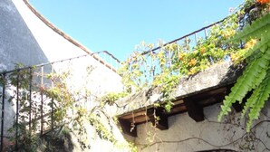 A rustic stone building with a wooden door and metal gate, surrounded by lush greenery and a stone staircase.