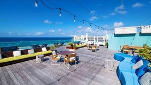 Une terrasse en bois avec des sièges extérieurs, une piscine et une vue sur l’océan.
