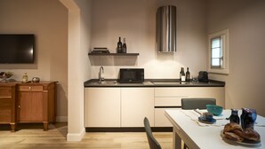 Cocina compacta con microondas, pileta y extractor de acero inoxidable. Se observa un mueble de madera y una mesa de comedor con productos para el desayuno.