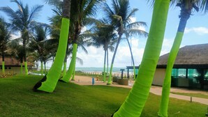 Ein tropisches Resort mit Palmen, Blick auf den Strand und einem Gebäude mit einem Reetdach.