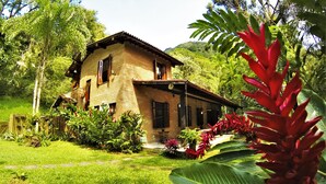 A two-story house with a brick exterior, surrounded by lush greenery and tropical plants. - Farmhouse on Félix Beach  (Ubatuba)