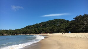 A beach with clear blue water, sandy shore, and a forested hill in the background. - Farmhouse on Félix Beach  (Ubatuba)