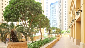 A corridor with potted plants and a palm tree, flanked by yellow buildings and tall structures in the background. - Pelicanstay Seaview Suites in JBR Walk (Dubai)