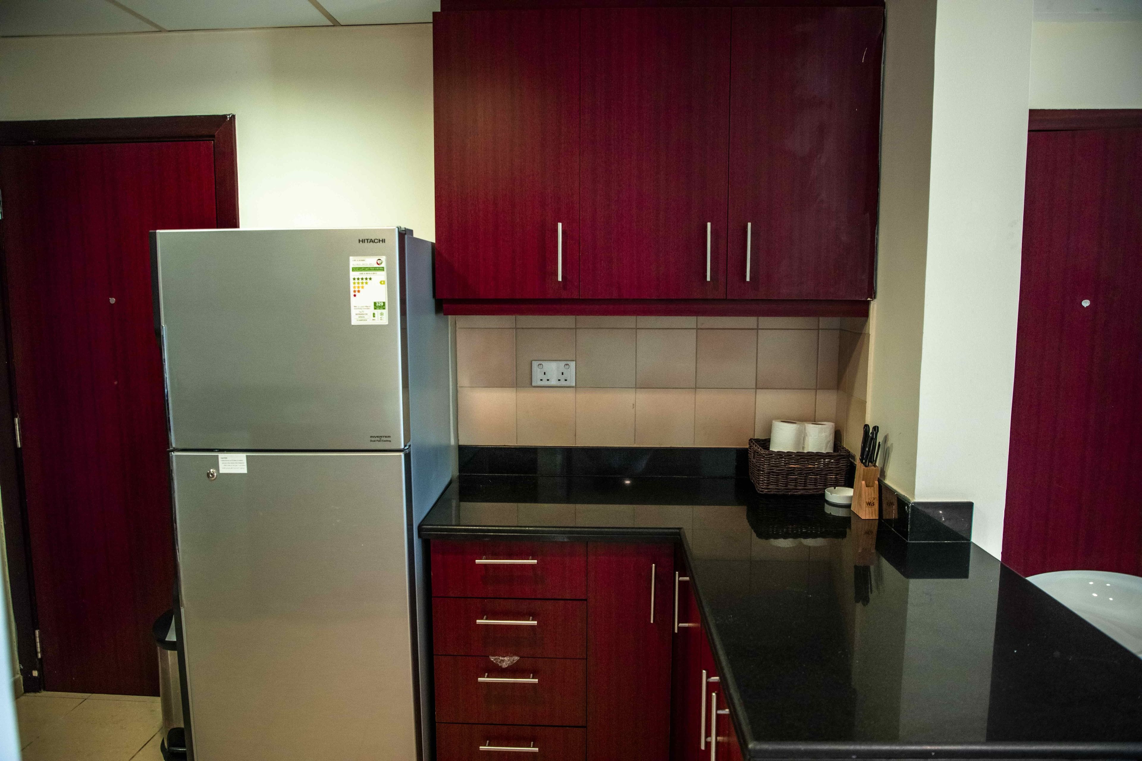 A compact kitchen with a refrigerator, wooden cabinets, and a black countertop.
