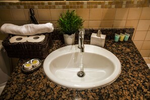 A bathroom sink with a white basin, a small potted plant, a basket with toiletries, and a towel on the counter.