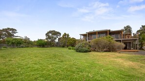 Una casa moderna de dos pisos amb un jardí espaiós i arbres madurs.