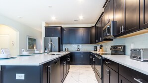 Une cuisine moderne avec des meubles de couleur sombre, un îlot central et des appareils électroménagers en acier inoxydable.