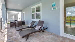 Een overdekt terras met rieten loungestoelen en een eettafel.