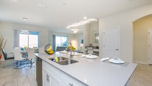A modern kitchen with a large island, stainless steel sink, and white cabinetry.