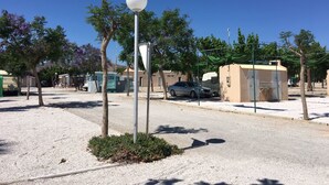 Un área de estacionamiento con un poste de luz esférico blanco, una carpa verde y un edificio color beige.