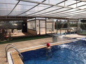 Una piscina interior con techo de vidrio, un trampolín y una cascada.