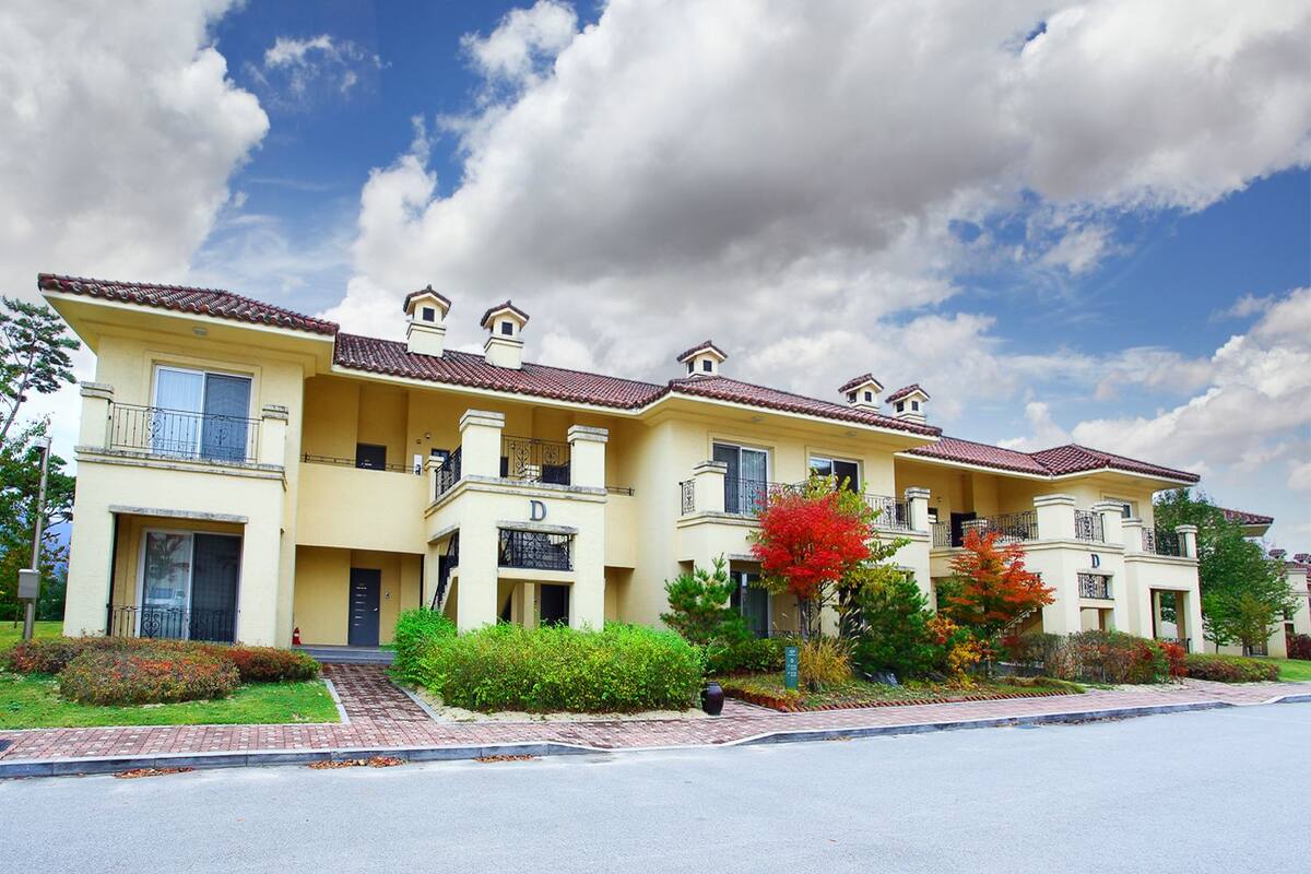 A row of two-story townhouses with balconies, a paved driveway, and a clear sky.