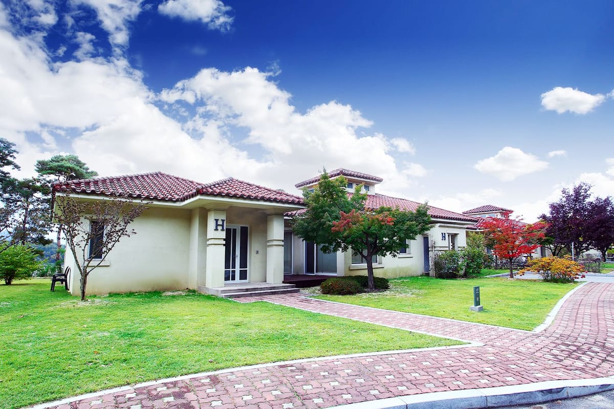 A two-story house with a tiled roof, a front porch, and a well-maintained lawn.