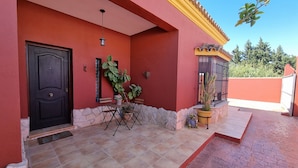 A red building with a black door, a small patio with a table and chairs, and a potted plant.