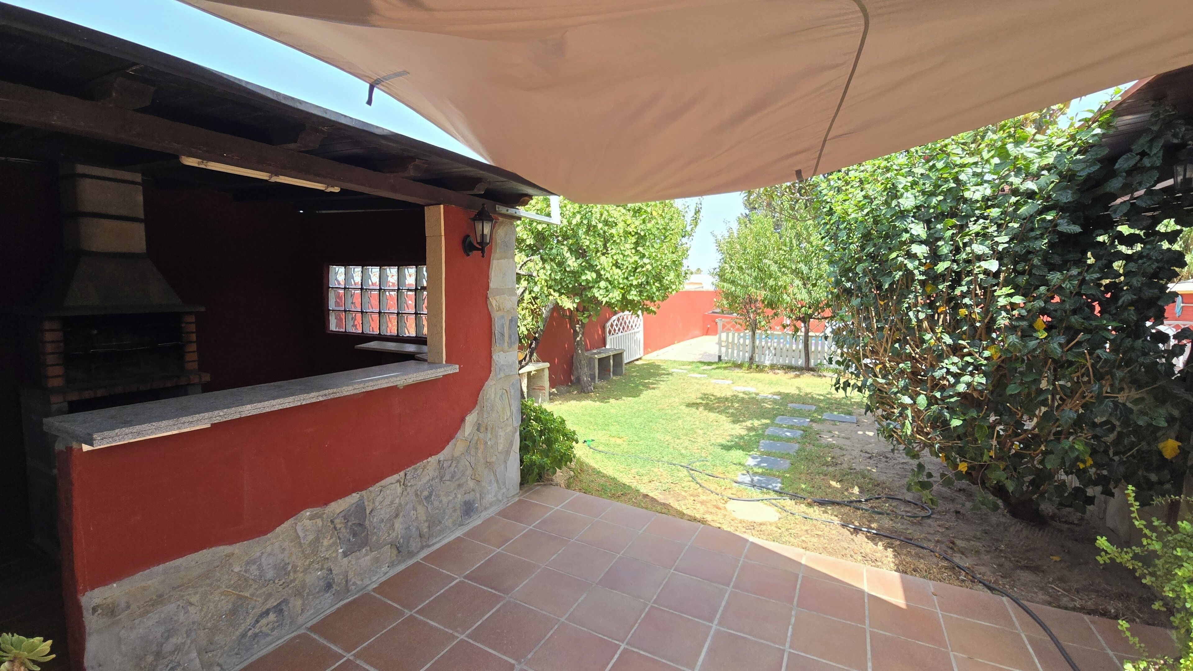 Eine Terrasse mit Steinplattenboden, einer roten Wand und einem Grill.
