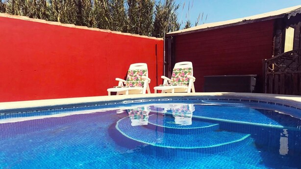 A swimming pool with two lounge chairs and a red wall.