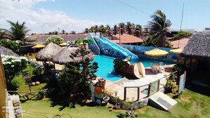 Zona de piscina con tobogán, cabañas de techo de paja y mobiliario exterior.
