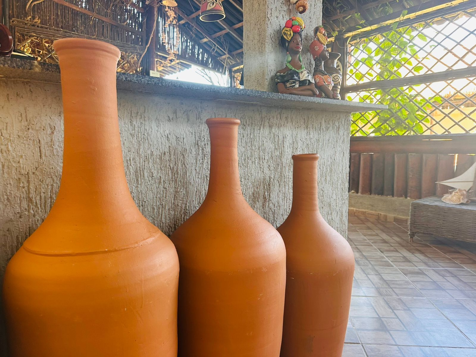 Trois vases en terre cuite de différentes tailles sont disposés sur un balcon doté d’une rambarde en bois rustique, et offrent une vue sur la verdure.