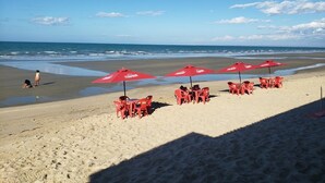 Una playa con sombrillas y sillas rojas, una orilla arenosa y el océano al fondo.