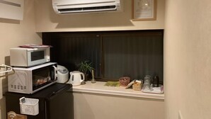 A compact kitchenette with a microwave, kettle, and small refrigerator. An air conditioner is mounted above the window, and a framed certificate hangs on the wall. - Fuu Tei (Kyoto)