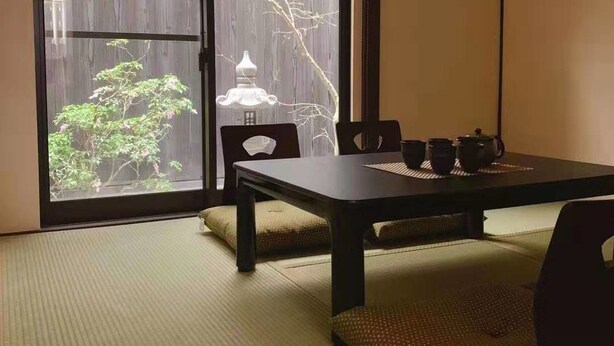 A traditional Japanese-style room with tatami flooring, a low table, and sliding doors leading to a view of a garden. - Fuu Tei (Kyoto)