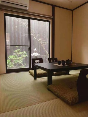 Una habitación tradicional japonesa con suelo de tatami, una mesa baja y puertas correderas que dan a un jardín.