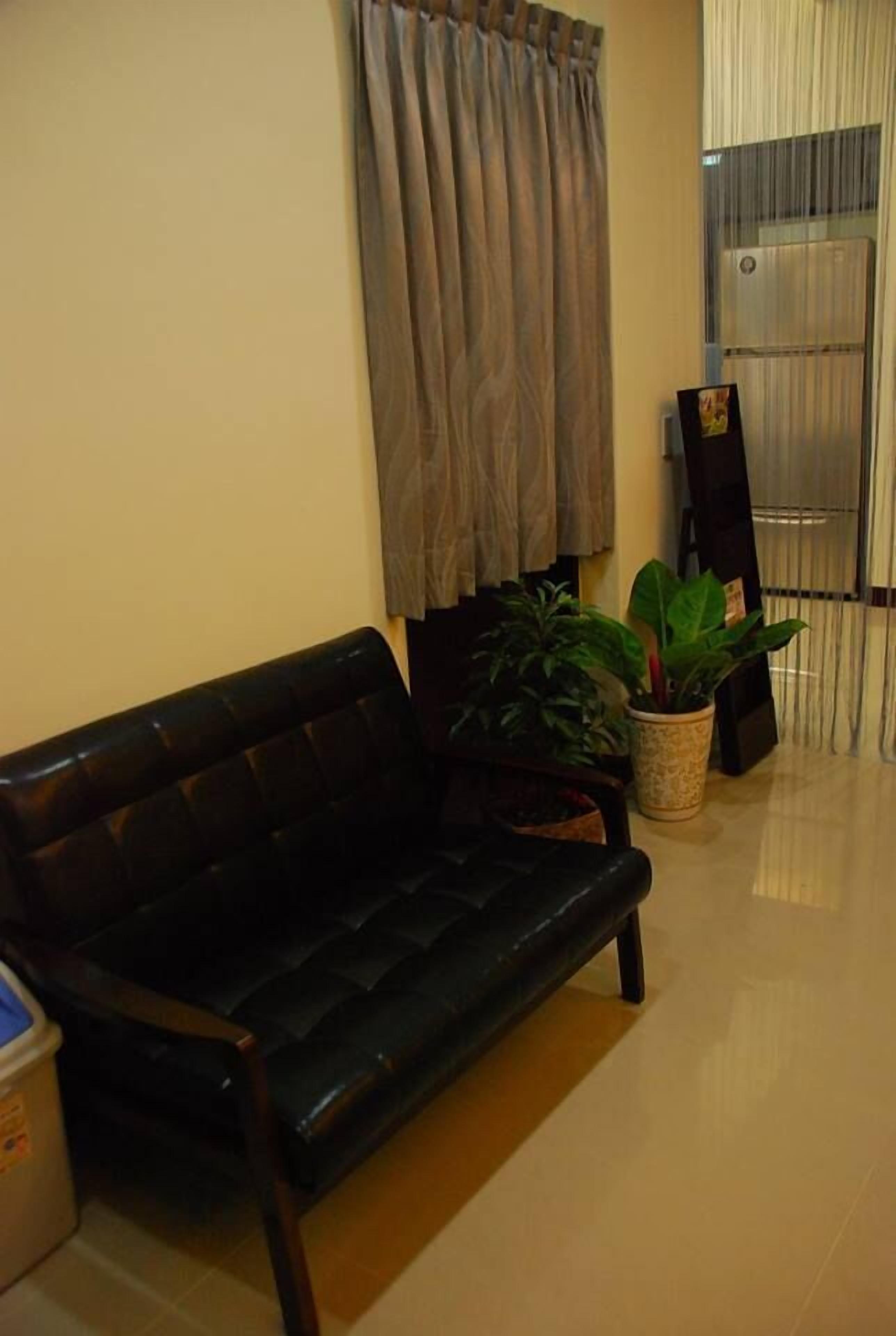 A black leather sofa, two potted plants, a wall-mounted TV, and a sliding glass door.