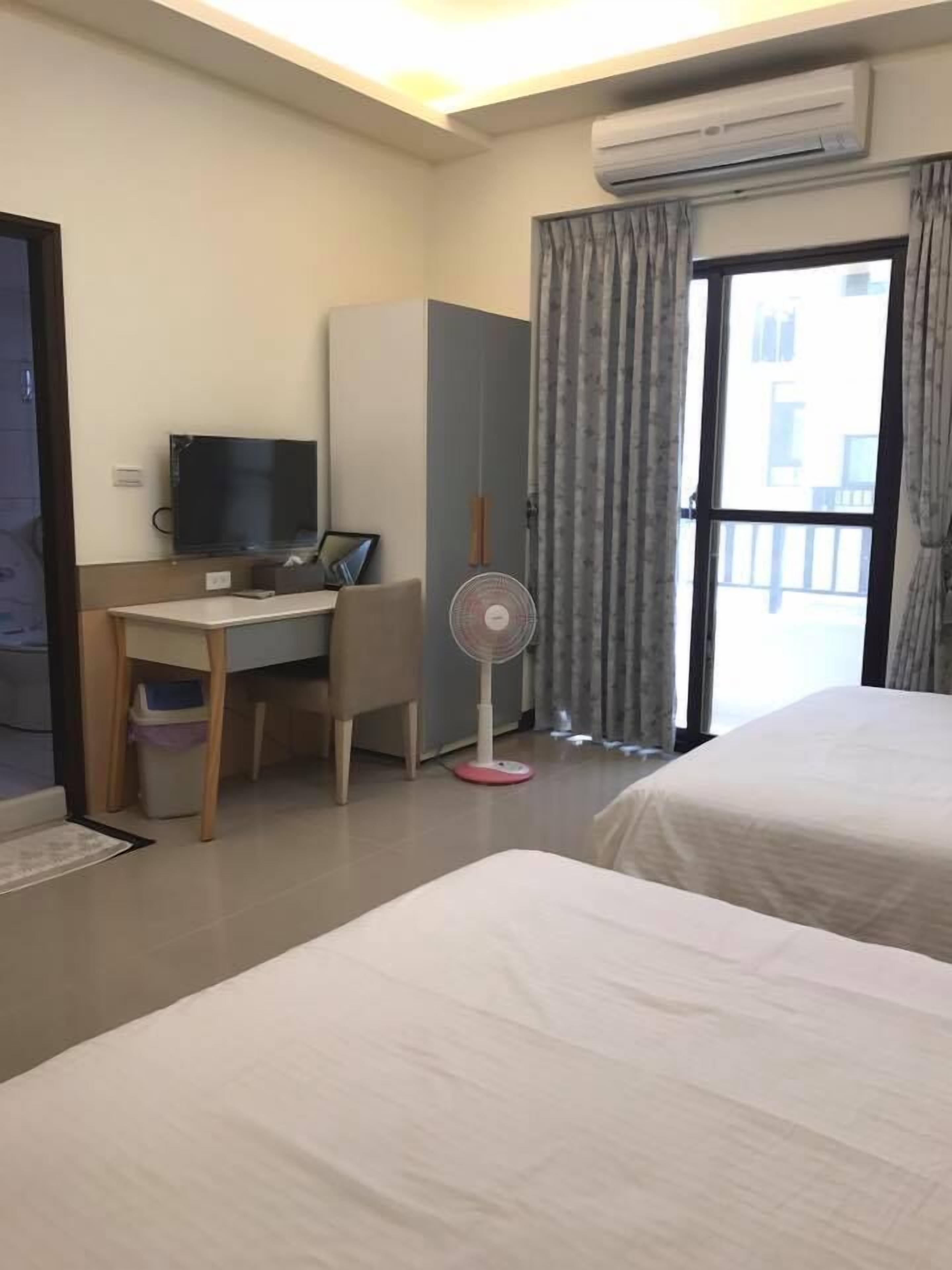 Een hotelkamer met twee bedden, een bureau met een computer, een ventilator en een airconditioning.