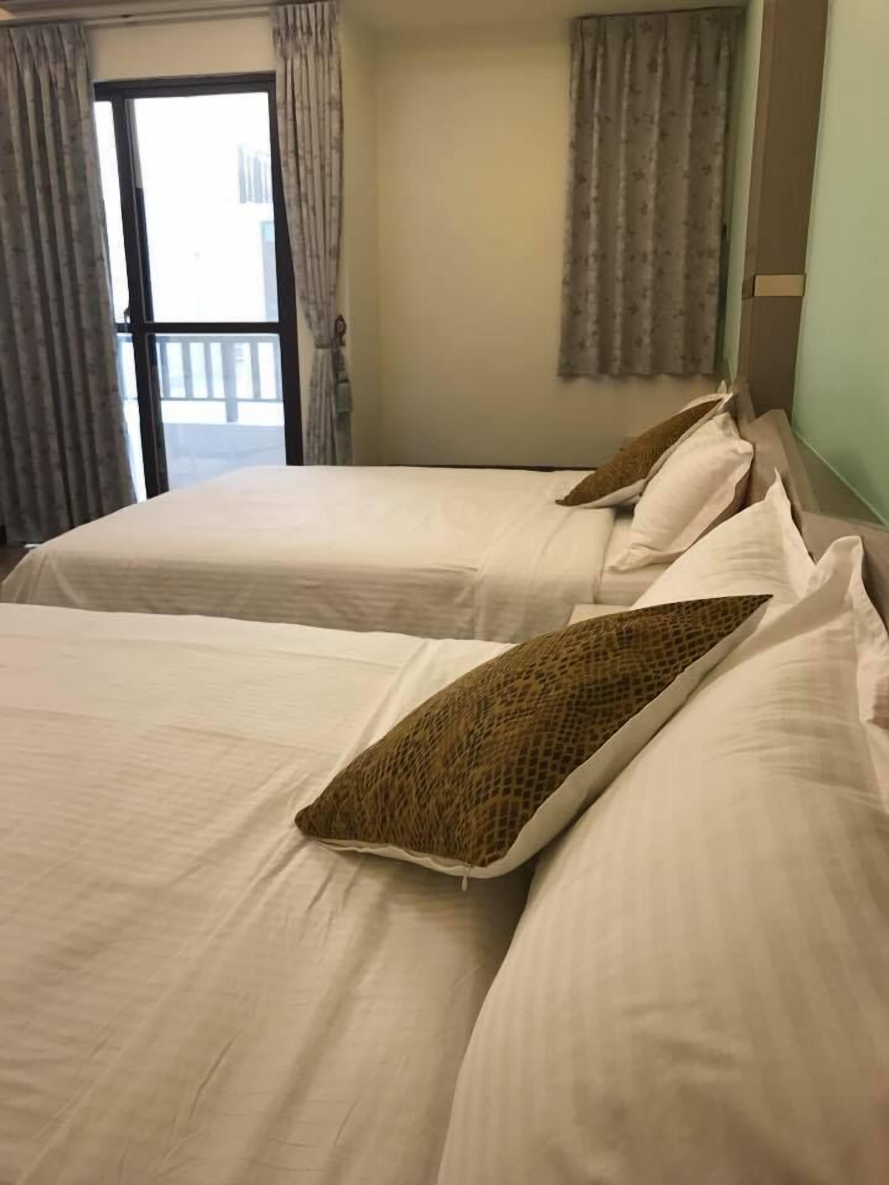 Habitación de hotel con dos camas, cada una con ropa blanca y almohadas estampadas.