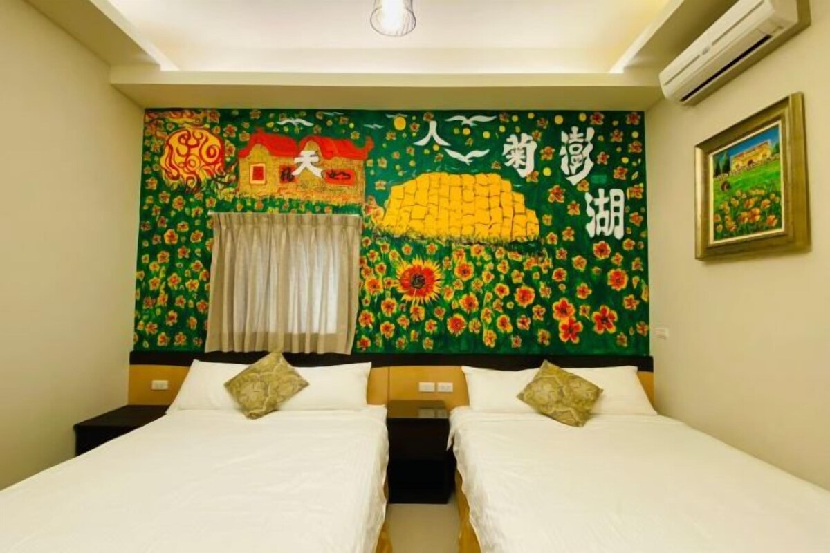 A hotel room with two beds, a green floral tapestry on the wall, a window with curtains, and an air conditioning unit.