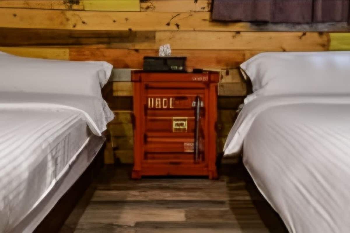 A room with two beds, a wooden wall, and a small red cabinet with a lock.