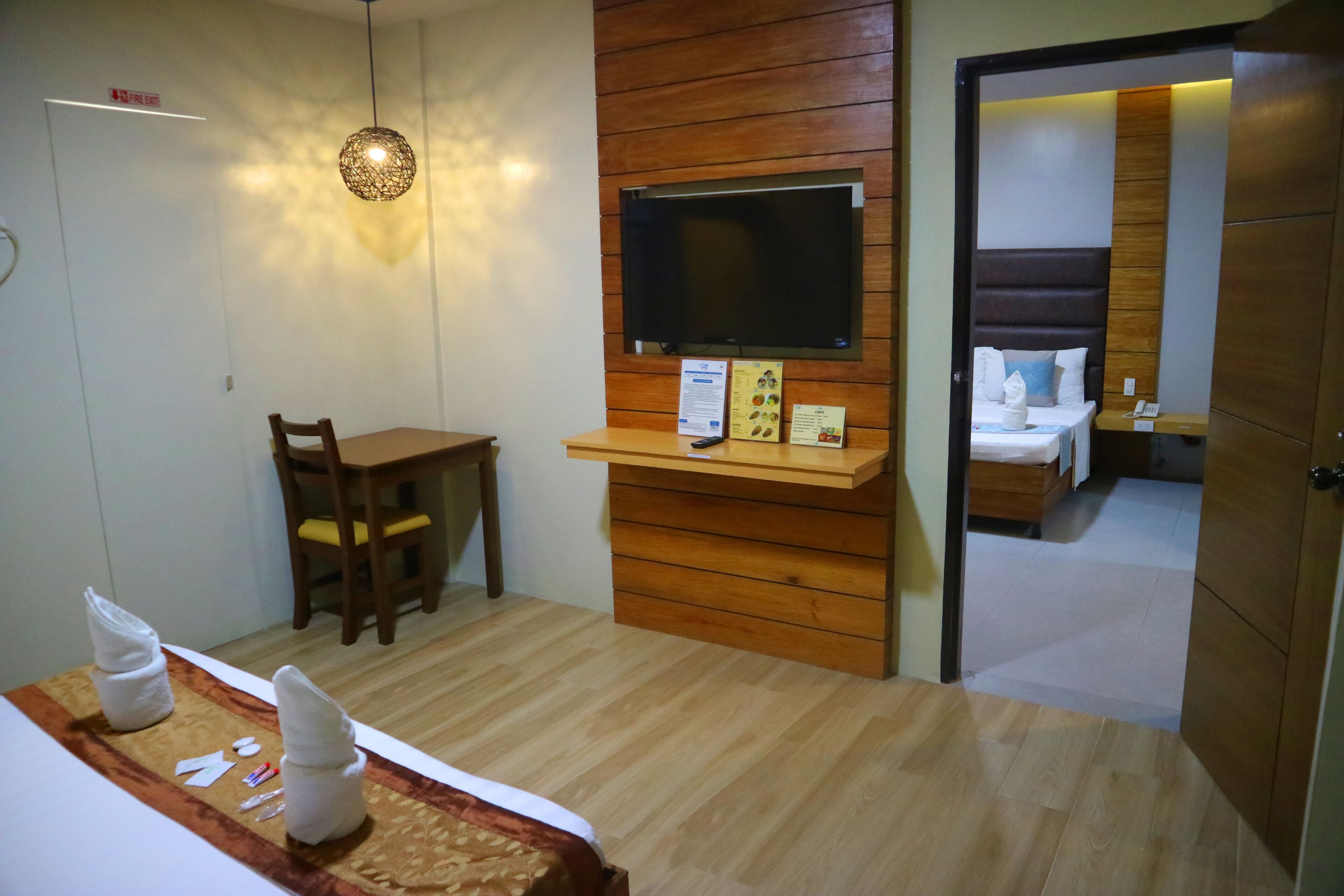A hotel room with a bed, a desk, a television mounted on the wall, and a wooden panel design.